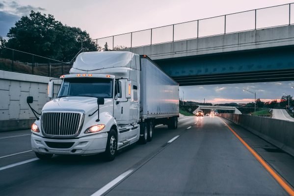 White 18 wheeler tractor trailer semi-truck on the highway at dusk