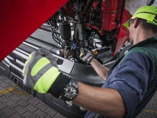 Truck Service Oil Level Check by Caucasian Worker Technician. Semi Truck Maintenance.